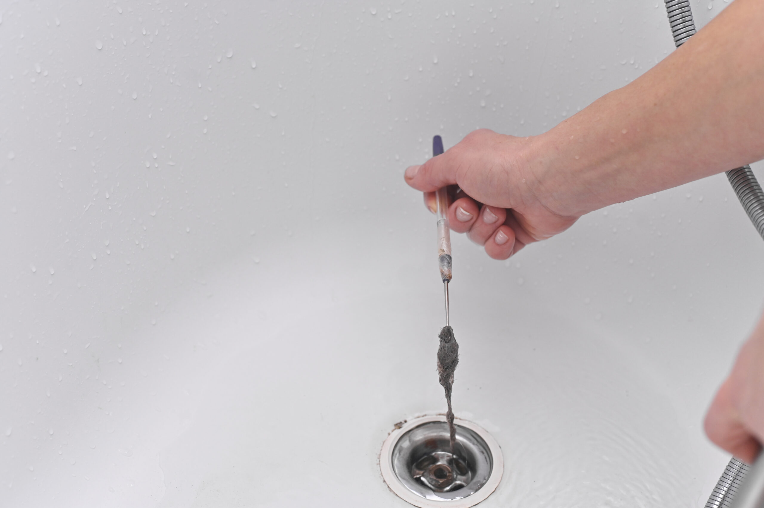 Person manually cleaning a bathtub drain with a small tool, removing a hair clog during a drain cleaning service in Conroe, Texas.