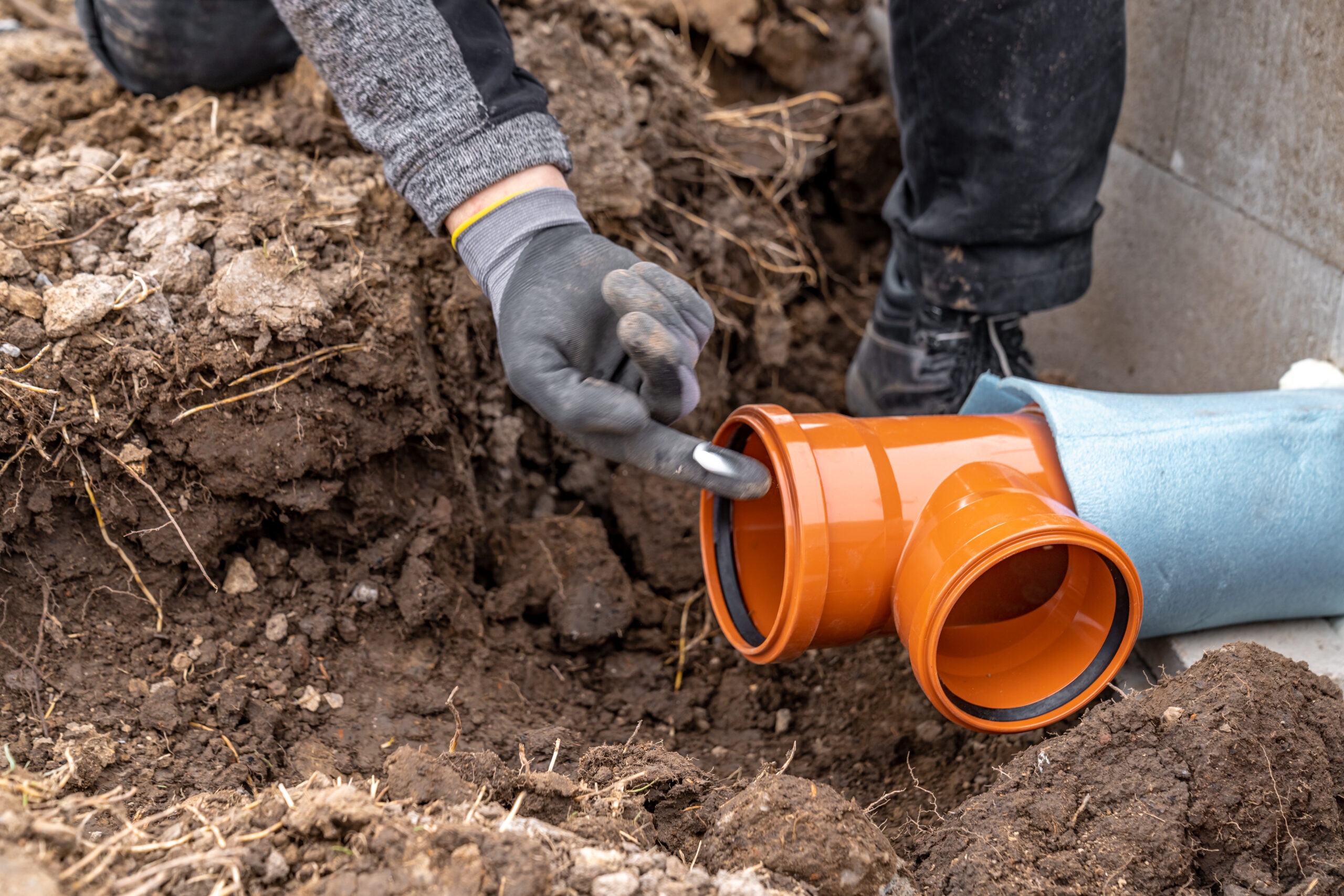 Plumber repairing an underground sewer line using orange PVC pipes during a sewer line replacement project in Conroe, Texas.